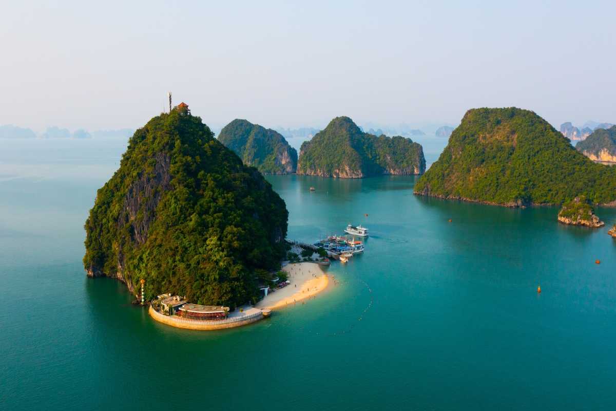 Ti Top Island’s lush limestone hill and sandy beach surrounded by turquoise waters in Ha Long Bay.