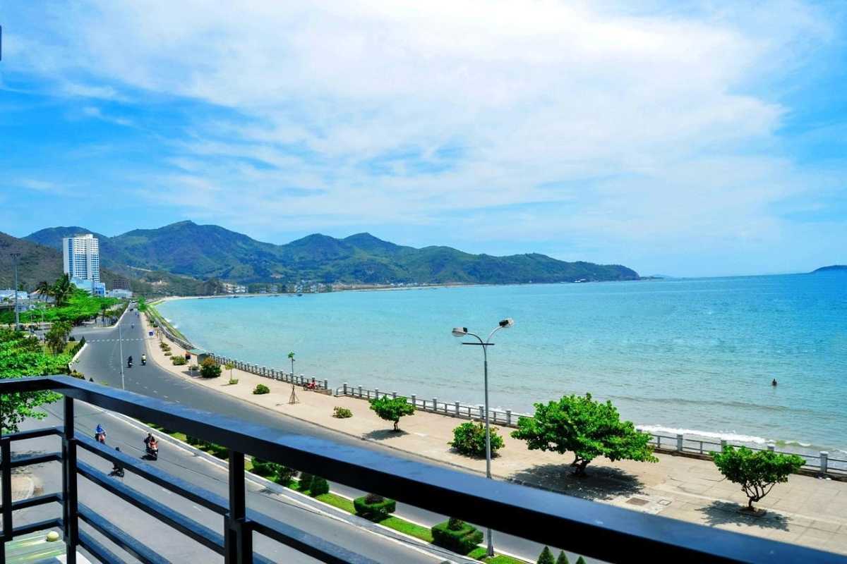 Aerial view of Tien Beach Nha Trang showing the beach, coastal road, and nearby town with mountains in the distance.