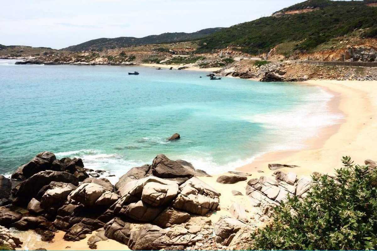 Pristine sandy shore of Tien Beach Nha Trang with clear blue waters and lush green hills in the background.