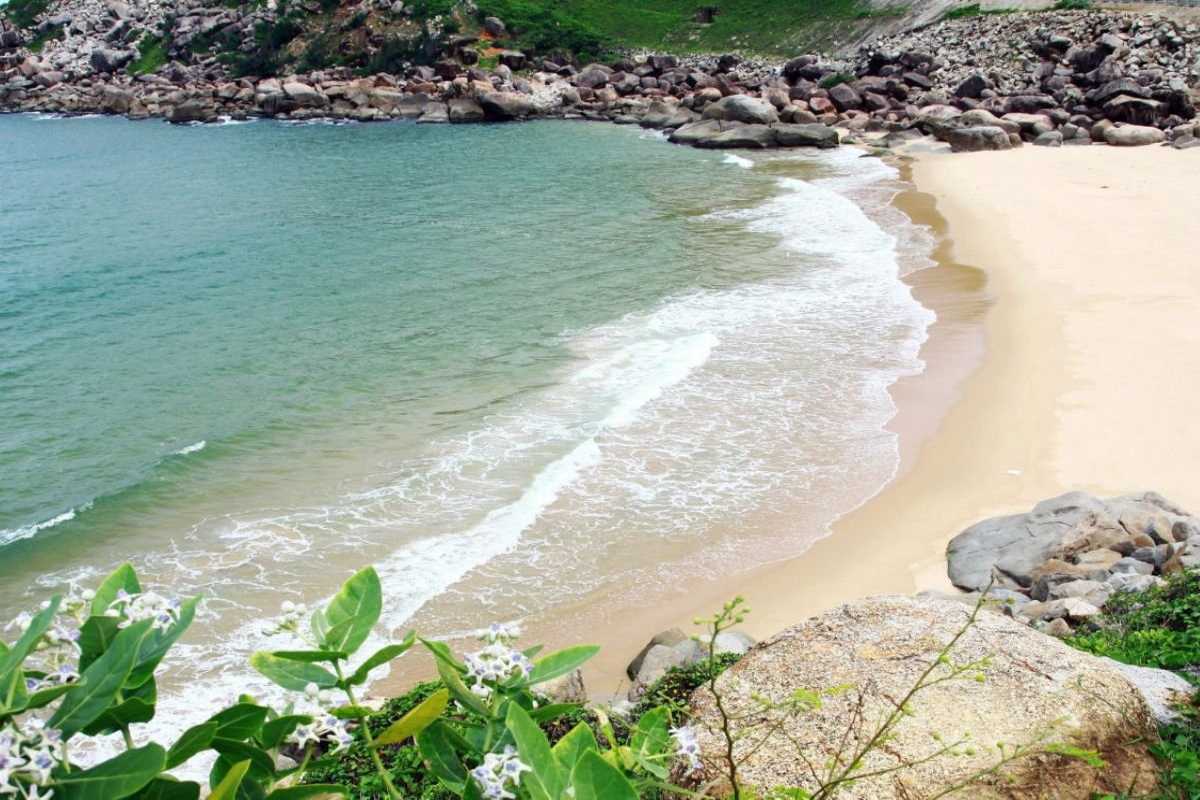 Natural rocky coastline and sandy beach at Tien Beach Nha Trang with green hills in the background.
