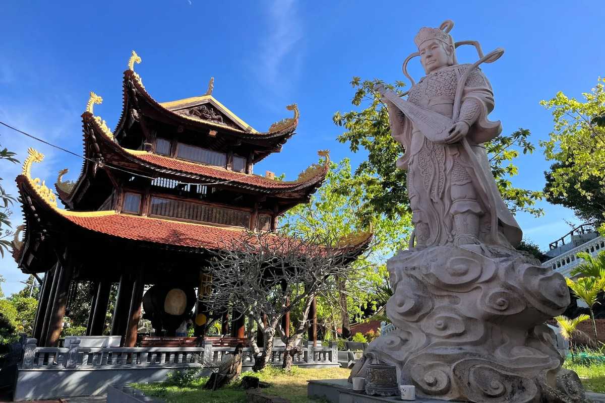 White statue and traditional pagoda buildings surrounded by lush greenery at Tong Lam Lo Son Pagoda