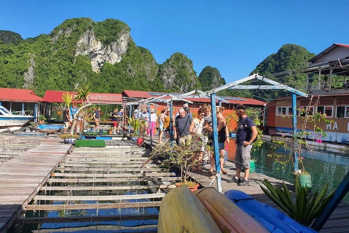 Tourists on small boats exploring the farm at Tung Sau Pearl Farm Halong Bay, with life jackets and limestone cliffs