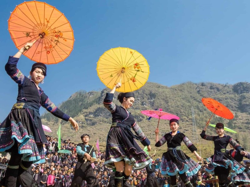 Hmong women in traditional attire performing a dance at Bac Ha Market Festival, holding colorful umbrellas