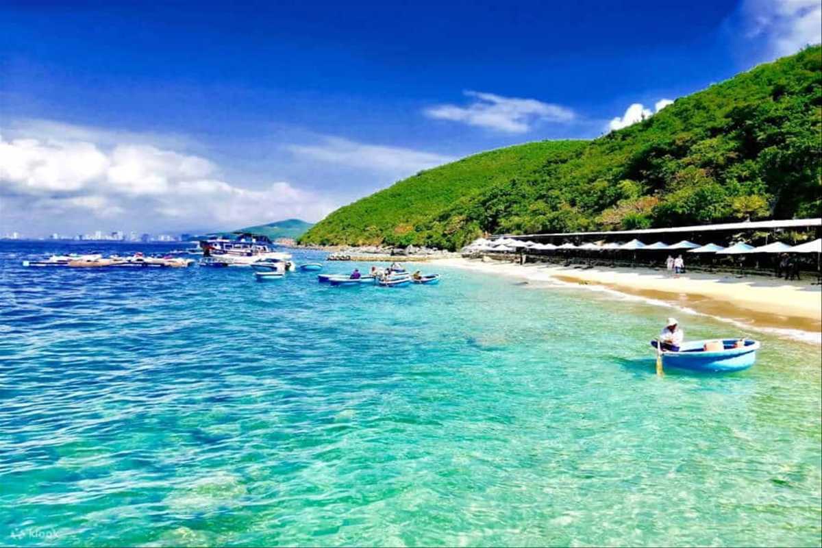 Clear turquoise waters and sandy shore at Tranh Beach Nha Trang with lush greenery in the background