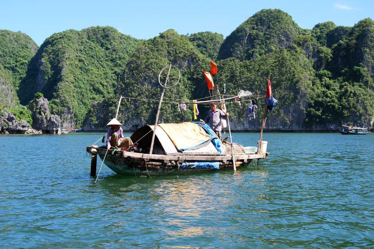 Tourists wearing life jackets on small boats at Tung Sau Pearl Farm Halong Bay with towering limestone cliffs in the background