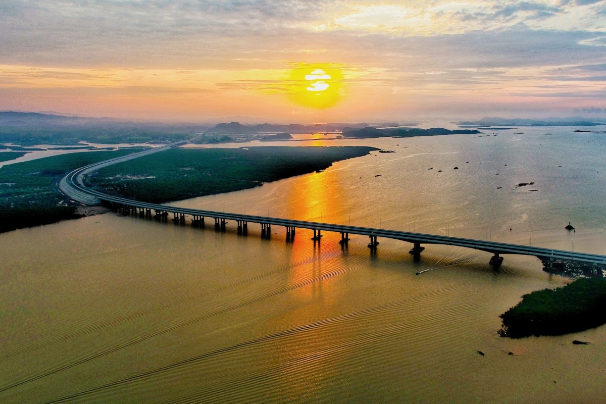 A stunning view of the Van Don to Mong Cai Expressway spanning the Red River at sunset, showcasing the golden hues reflected on the river.
