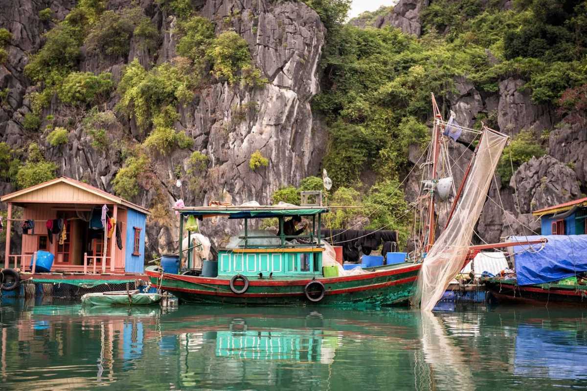 Traditional fishing boat moored at Vung Vieng Fishing Village with lush limestone cliffs in the background