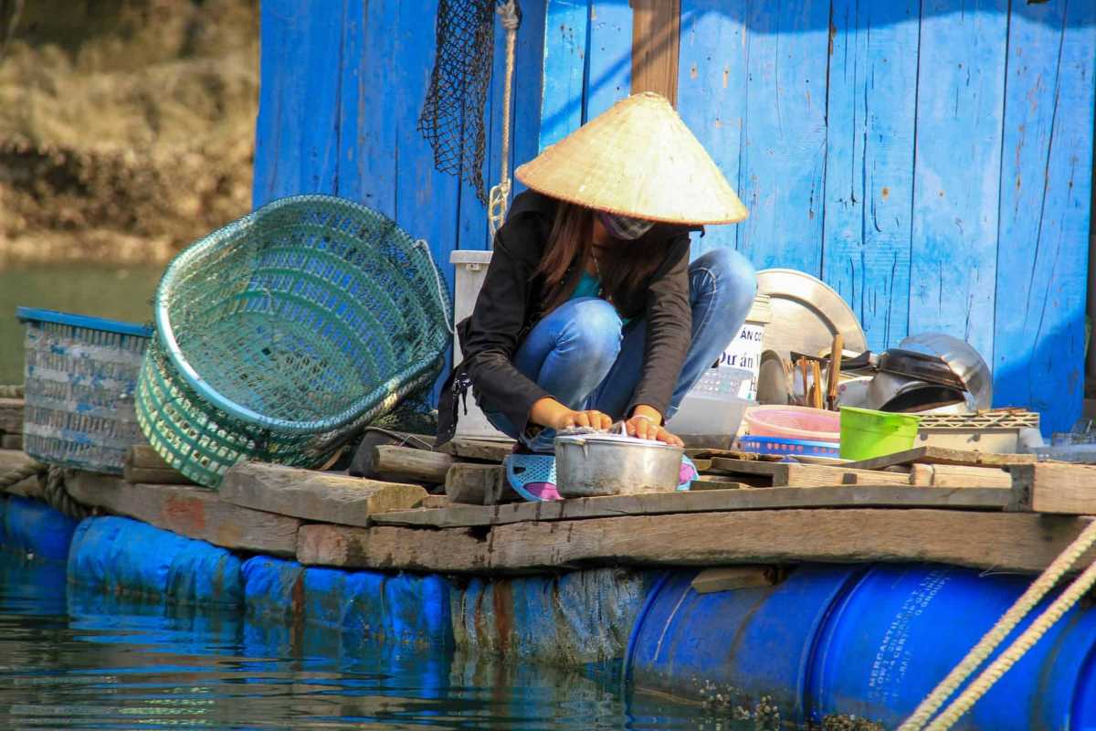 Resident washing utensils on floating home deck at Vung Vieng Fishing Village on Halong Bay