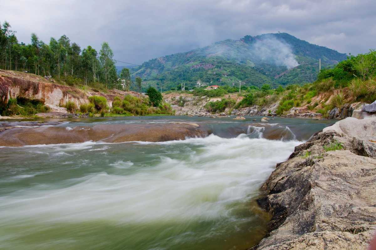 Natural rapids at Waterland Thach Lam Mountain-fed stream flowing over large rocks at Waterland Thach Lam with dramatic backdrop.