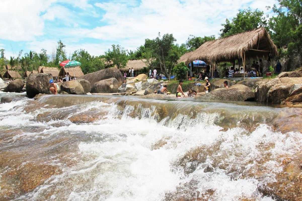 Picnic huts by the stream at Waterland Thach Lam Families relaxing in huts and wading in shallow water along the stream edge at Waterland Thach Lam.