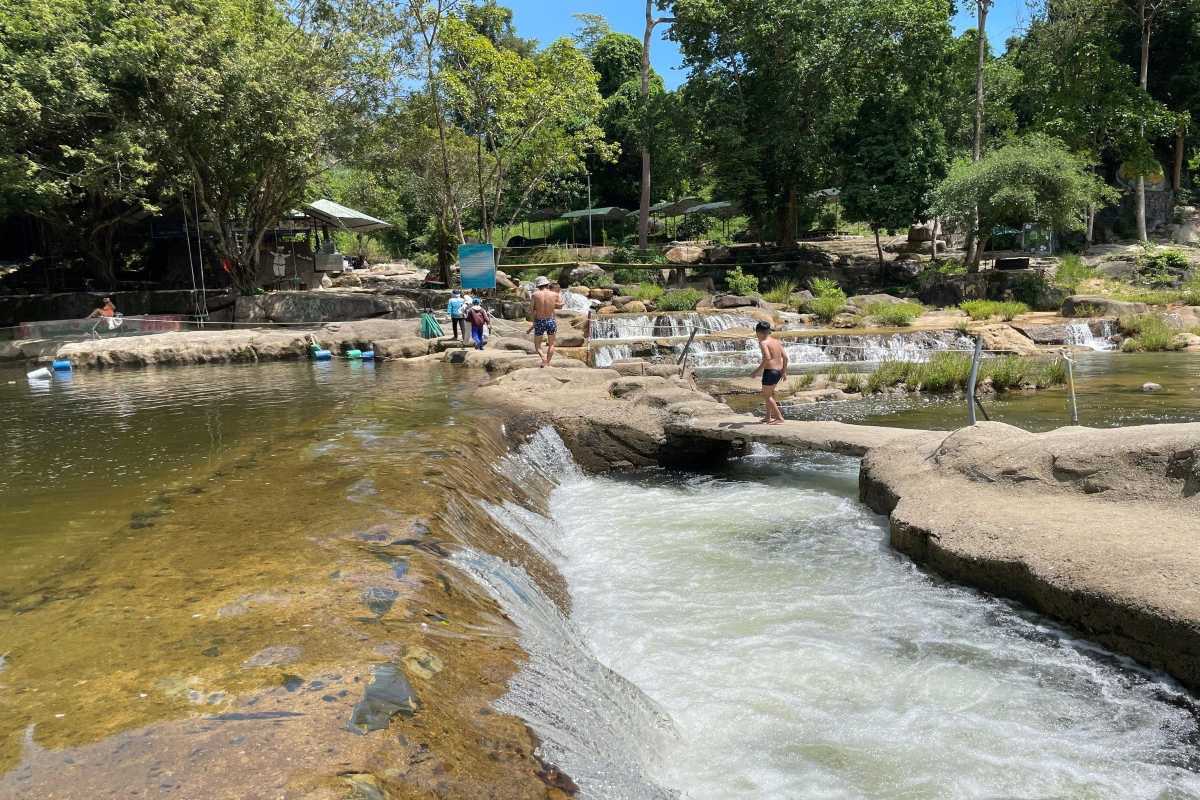 Visitors wade and swim in the natural pool at Yang Bay Waterfall surrounded by shaded forest