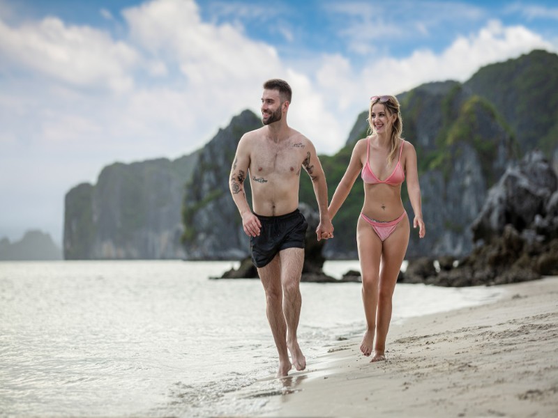 Couple in swimwear jogging along the beach in Ha Long Bay with cliffs in the background