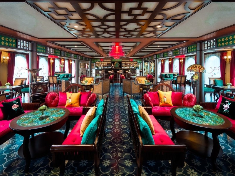 Stylish Cochinchine Lounge on Indochine Premium Cruise featuring vintage decor, vibrant seating, and sweeping views of Ha Long Bay.