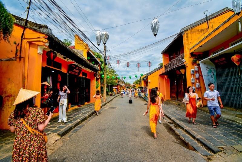 Street Life in Hoi An Ancient Town Tourists walking along a colorful street in Hoi An Ancient Town, showcasing the lively culture and traditional yellow-walled houses.