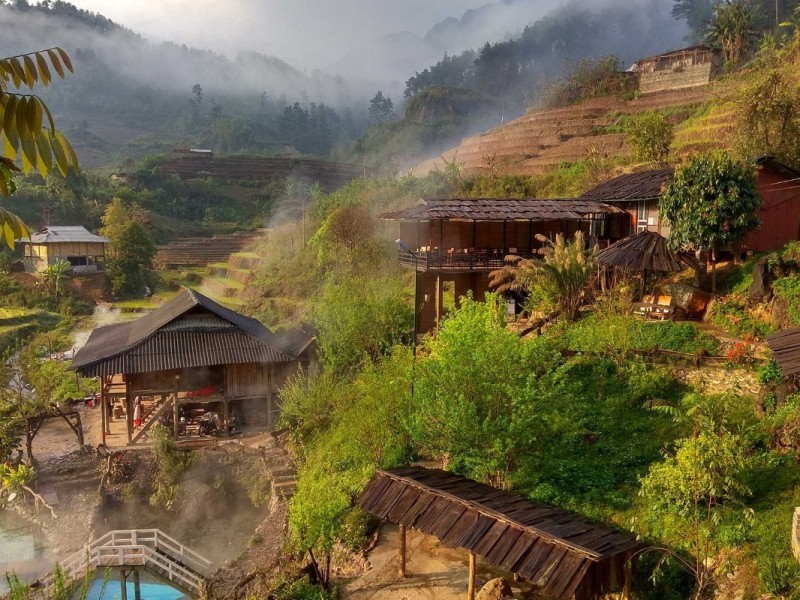 Tram Tau Hot Spring Homestay Steam rising from a traditional homestay at Tram Tau Hot Spring, surrounded by terraced fields.