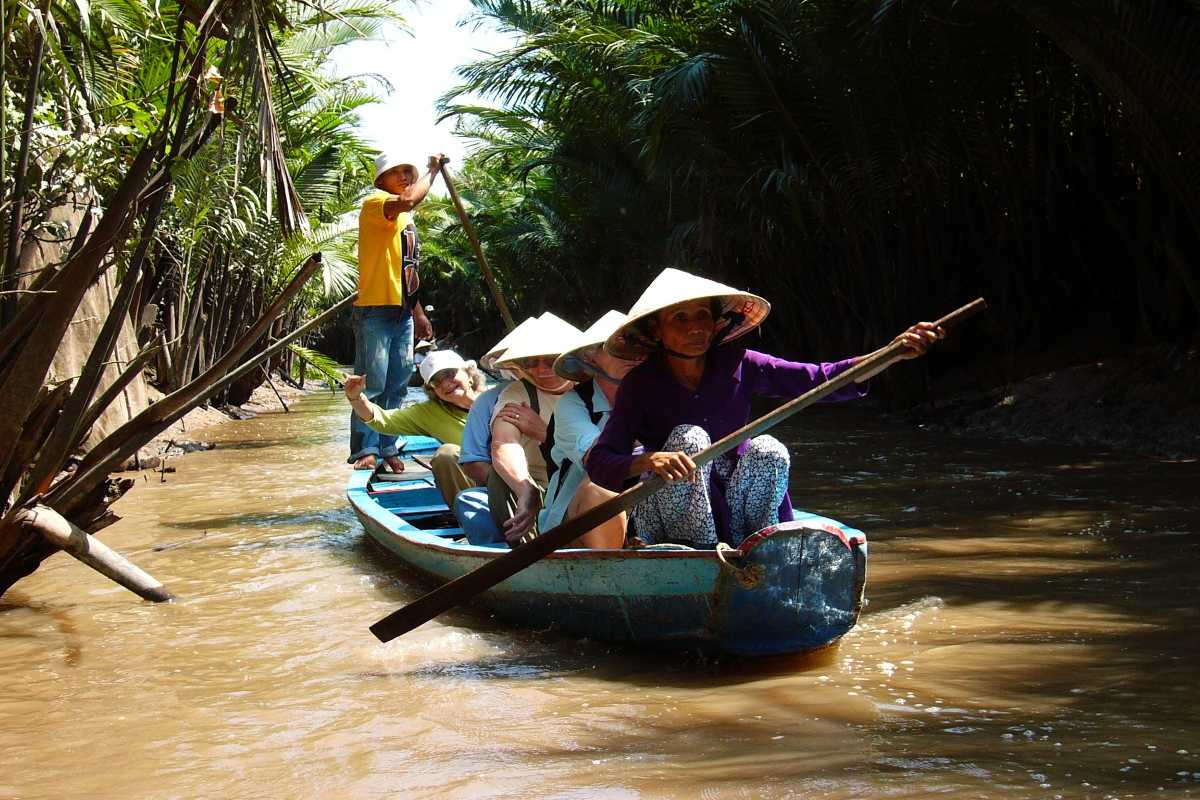 Vinh Long Mekong Delta boat tour with locals Vinh Long Mekong Delta boat tour showing locals rowing traditional wooden boats through lush waterways surrounded by dense greenery