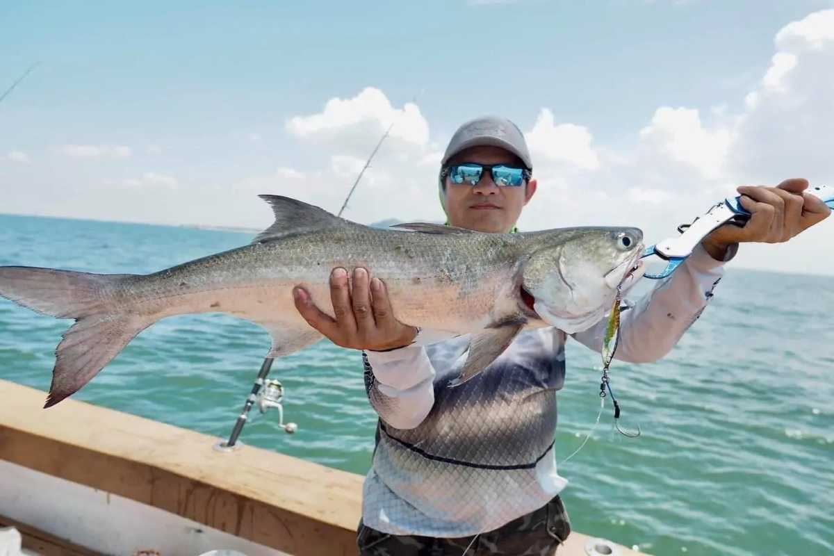 An angler proudly holds a large silver fish caught on the Nha Trang fishing tour against a scenic ocean backdrop.