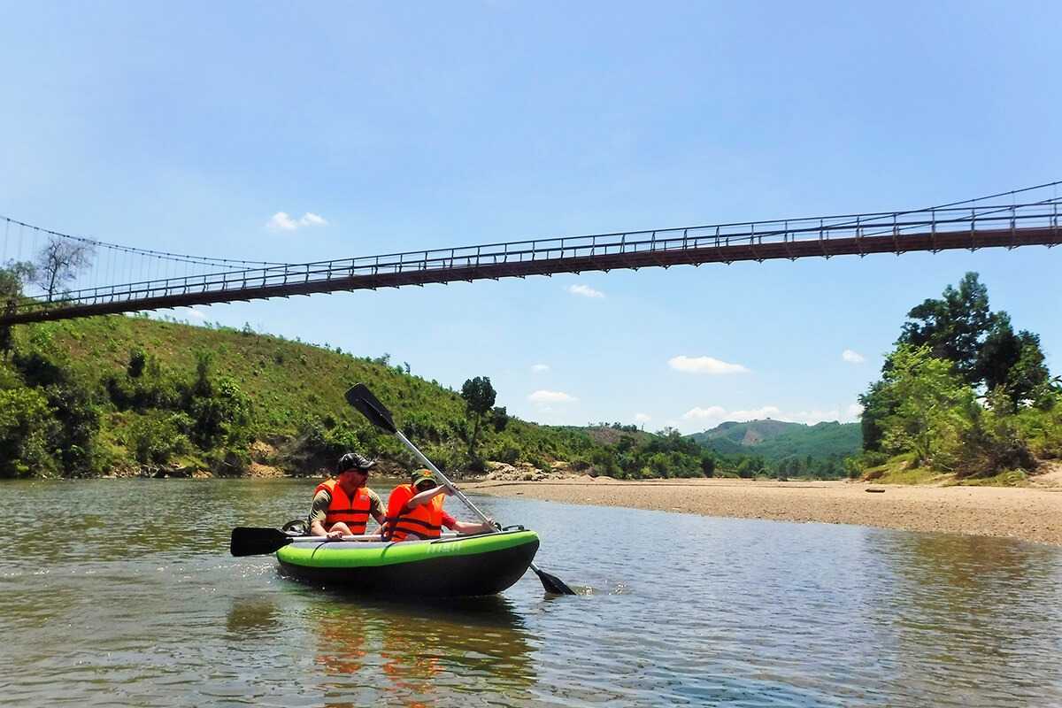Kayakers paddling near a suspension bridge on the Cai River in a remote Vietnam valley