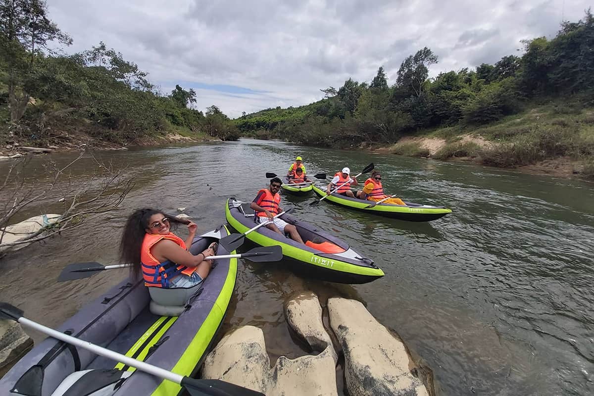 A group of tourists in inflatable kayaks resting and chatting near river rocks during a Nha Trang rafting trip.